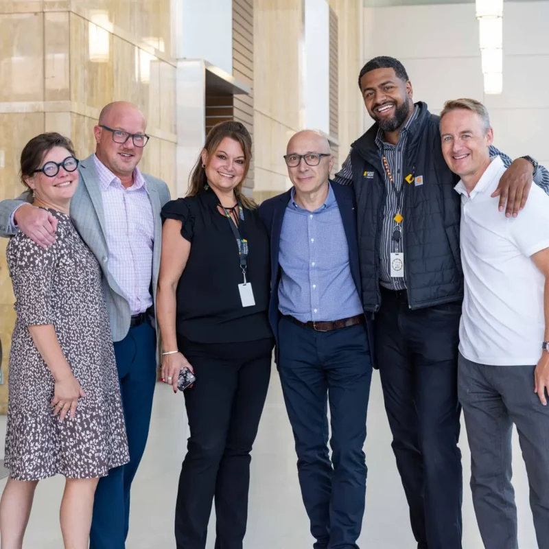 Group photo of Surerus Murphy Joint Venture team in a bright foyer of a large building in Calgary, showcasing professional corporate photography services.